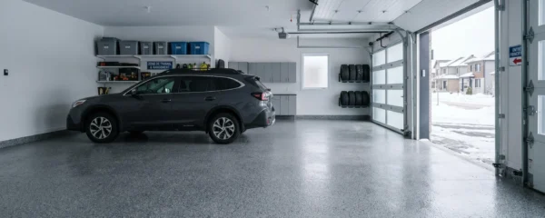 Garage résidentiel québécois moderne avec plancher en revêtement époxy-polyuréa gris à flocons granit, surface brillante et impeccable, véhicule récent stationné, lumière naturelle hivernale douce